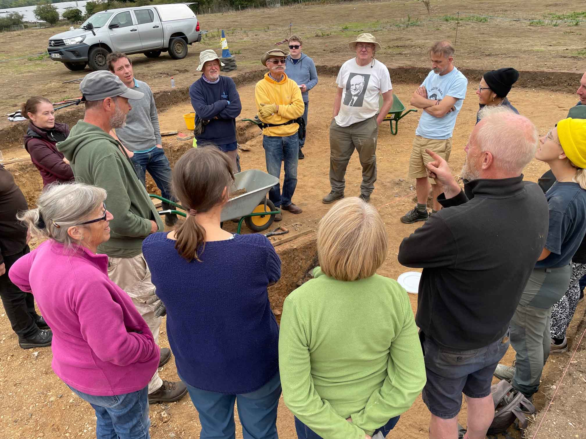 A group of people standing around an archaeological excavation pit.
