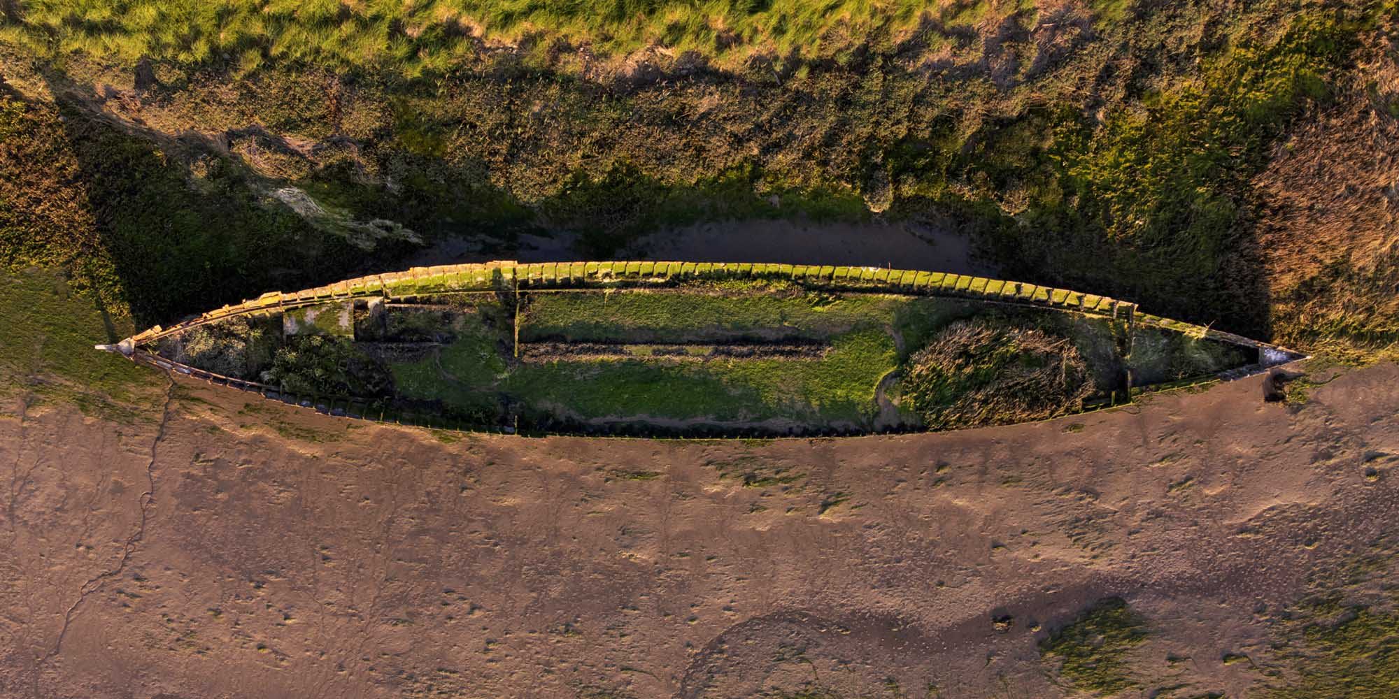 A birds-eye view of a wrecked ship on a muddy shore. 