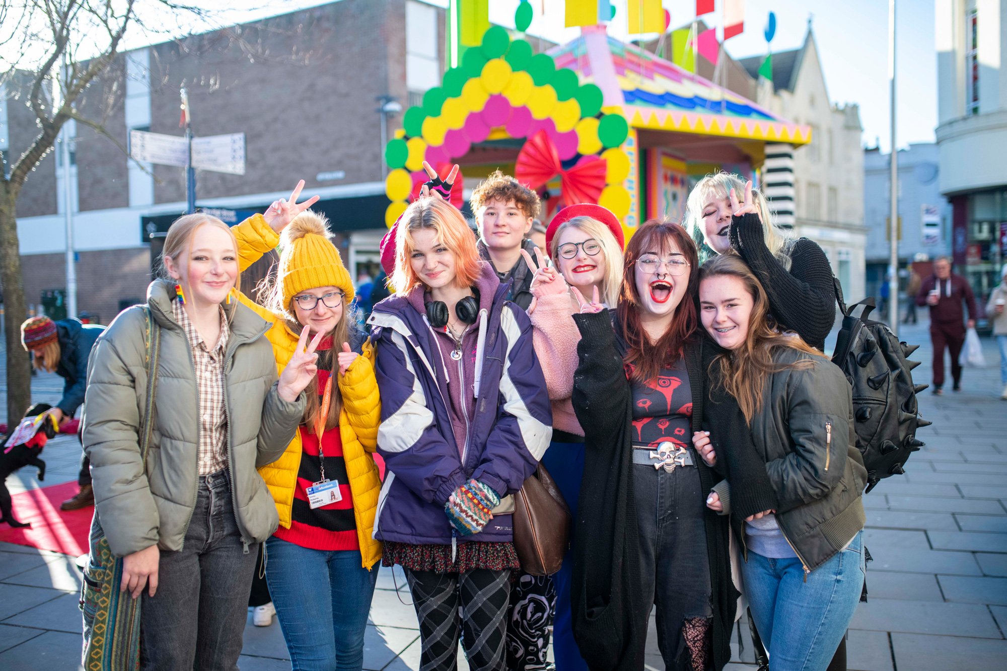 Group of young people pose for photo in front a colourful temporary shrine on a high street.