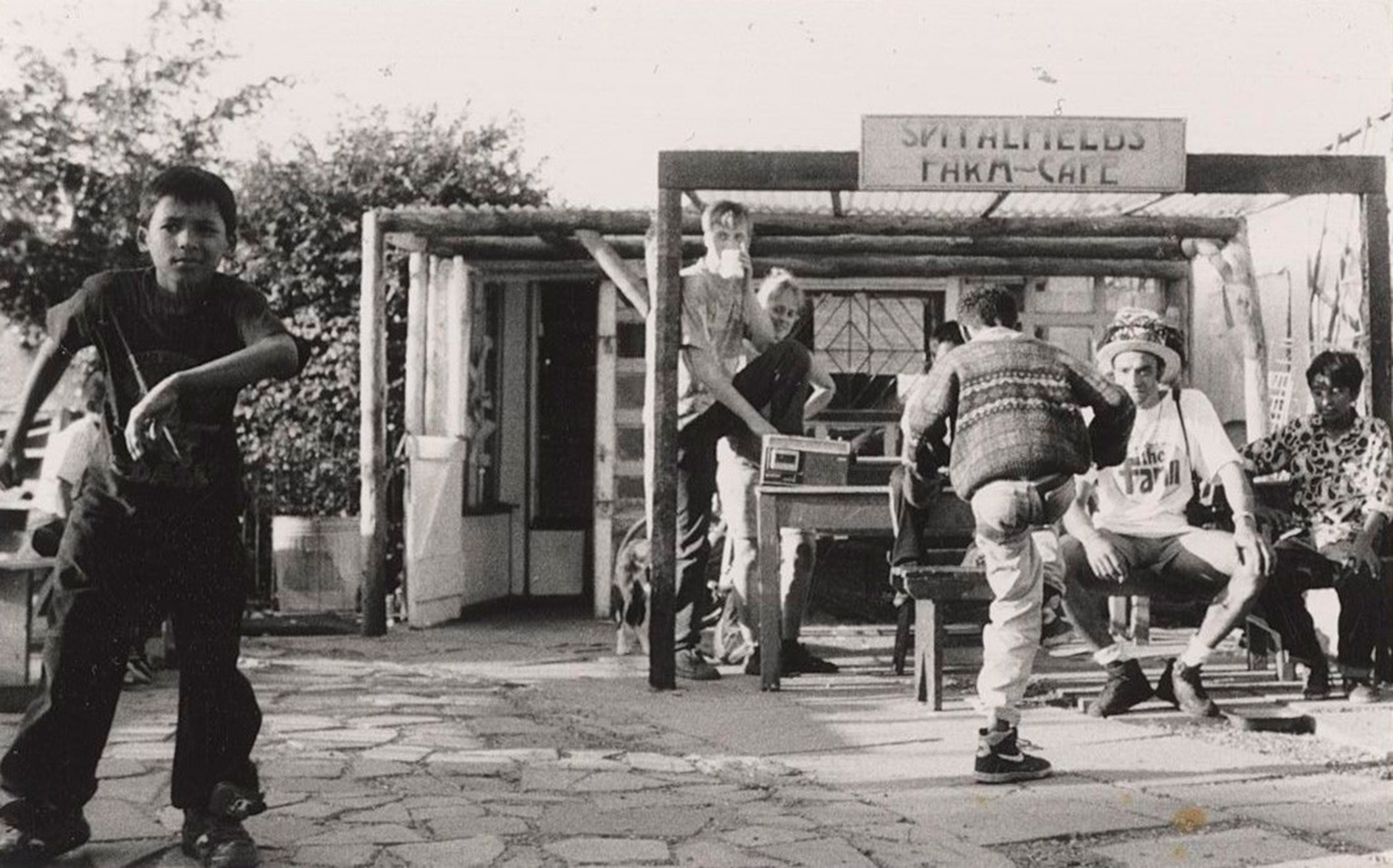 A black and white photo of a group of children dancing and sitting at a farm cafe, including a Bengali boy in the foreground.