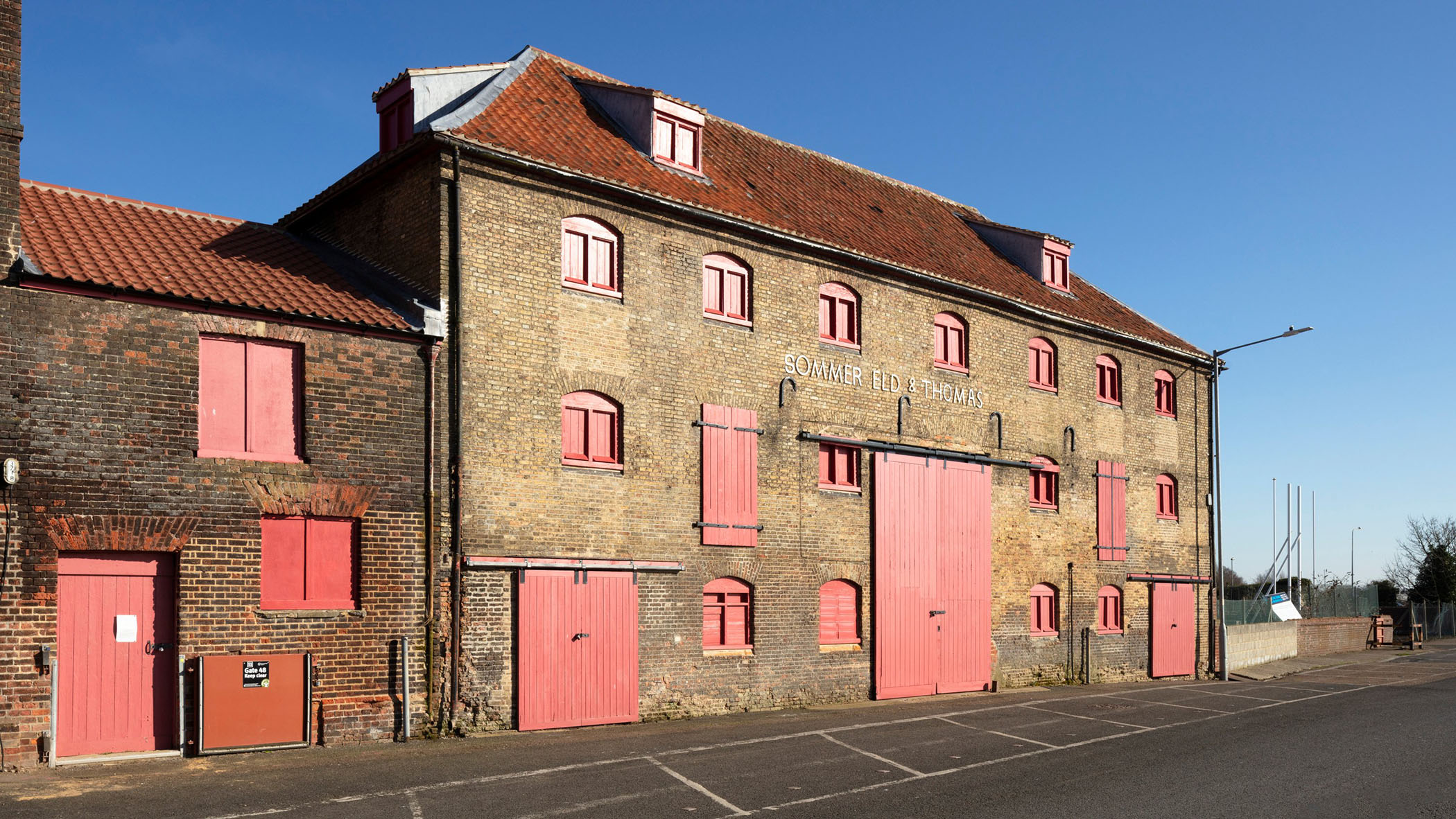 A large brick building with red windows and doors next to a road. 