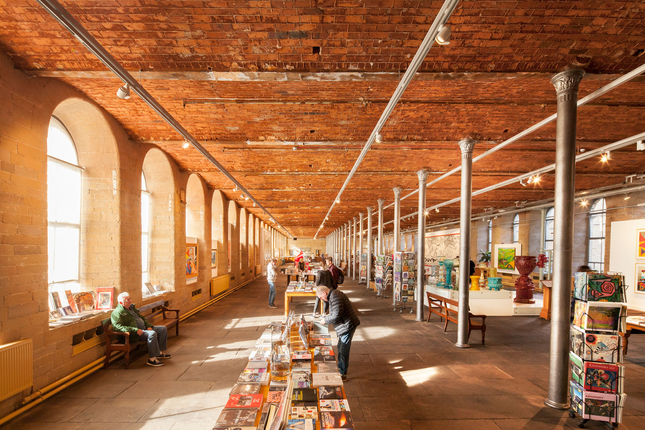 A photograph of people browsing in a bookshop with arch windows, columns, and a red brick ceiling overhead.