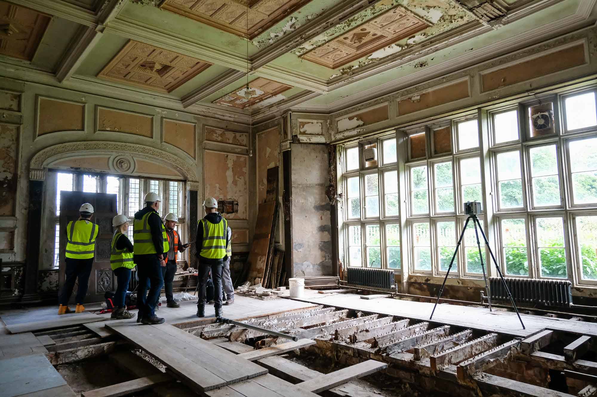 People stand at one end of a room with windows running the length of the room and exposed floor joists.