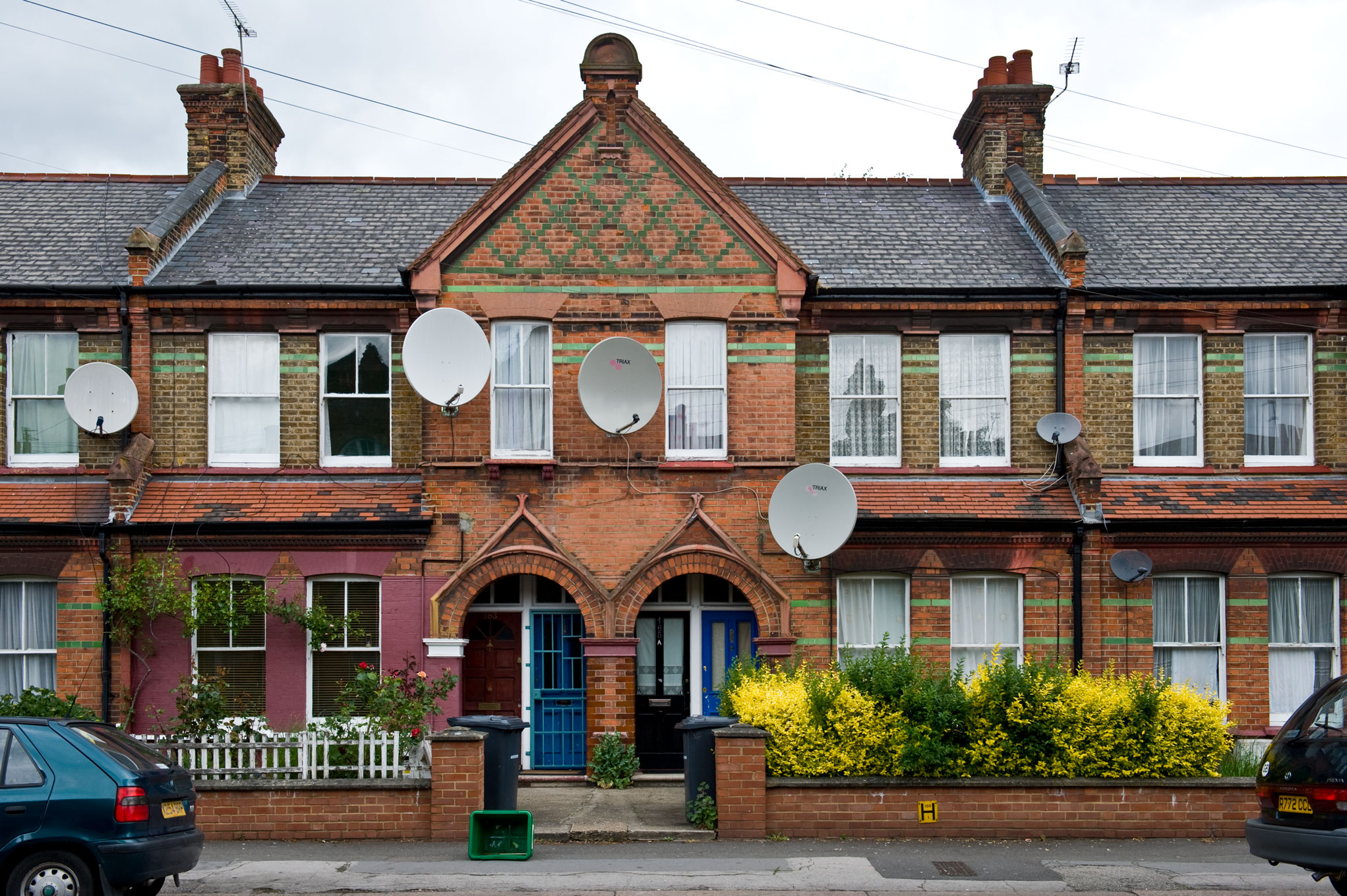 Colour photograph of a row of two storey brick houses to which satellite dishes have been attached.

