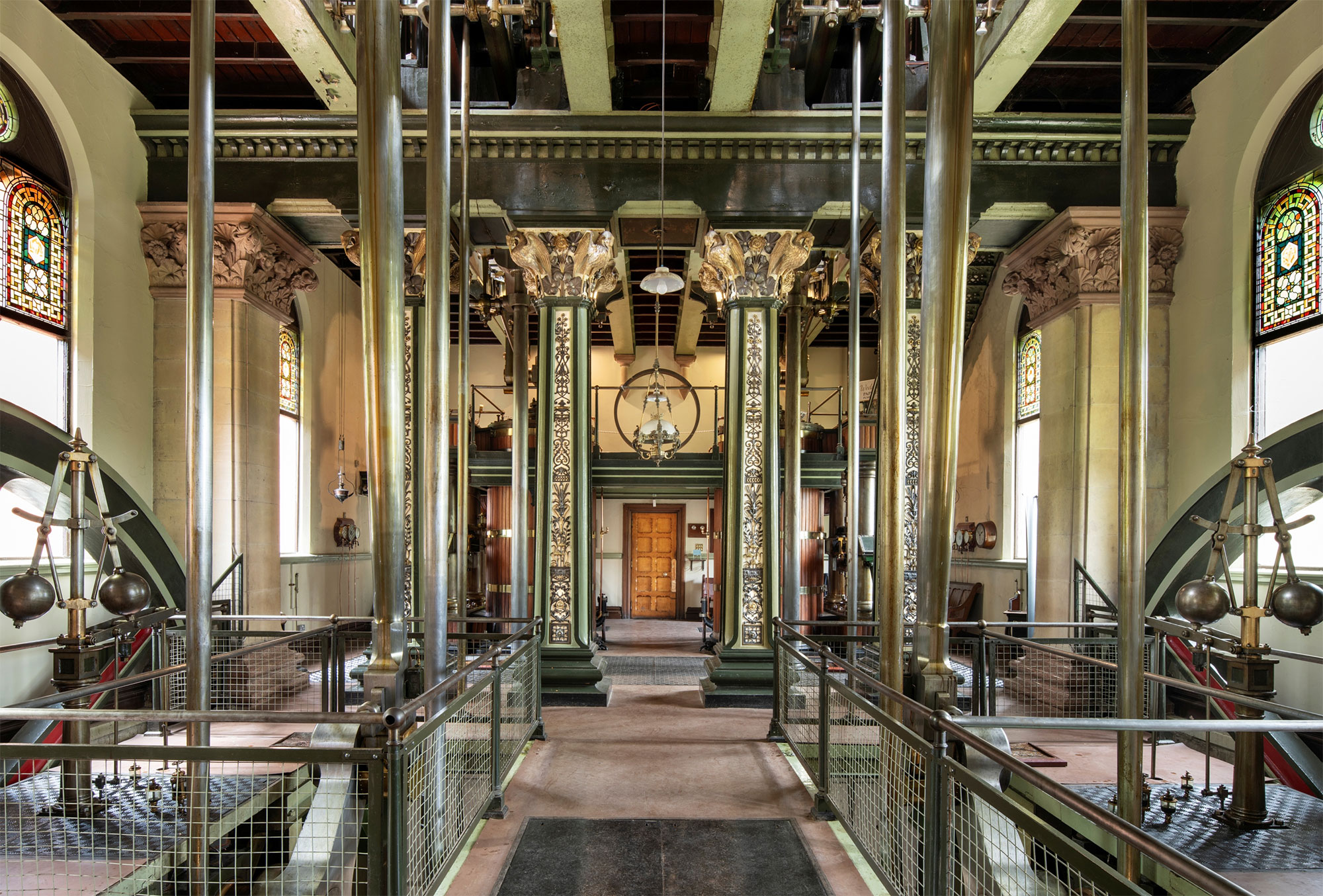 Inside of a pumping station room with intricate detail on green pillars around the room and equipment on both sides.