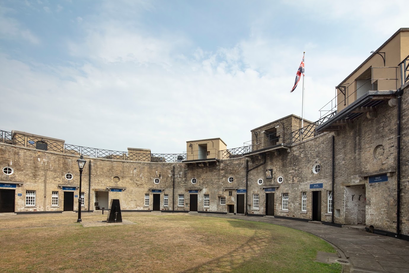 A semi-circle of stone buildings with wrought iron railings at top level and green space in front 