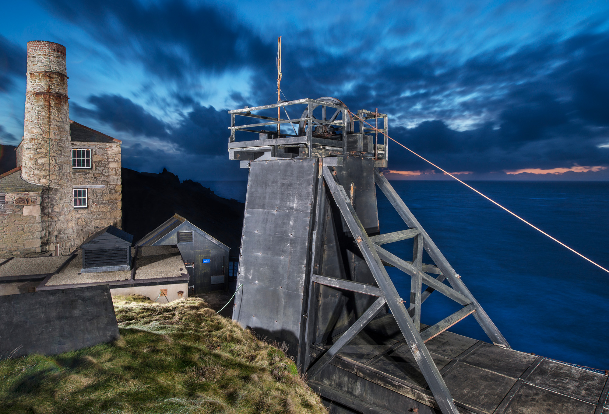 General view of engine houses and a headframe illuminated at dusk against a dramatic dark blue sky