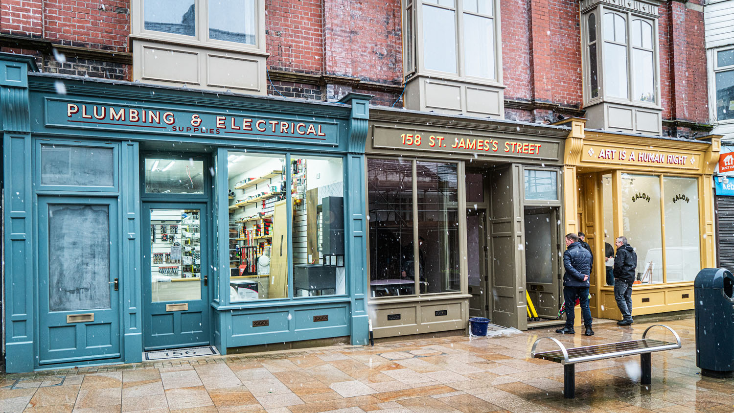 A group of 3 shops with newly restored and colourful shopfronts. Shop names include:
PLUMBING & ELECTRICAL SUPPLIES
158 ST. JAMES'S STREET
ART IS A HUMAN RIGHT