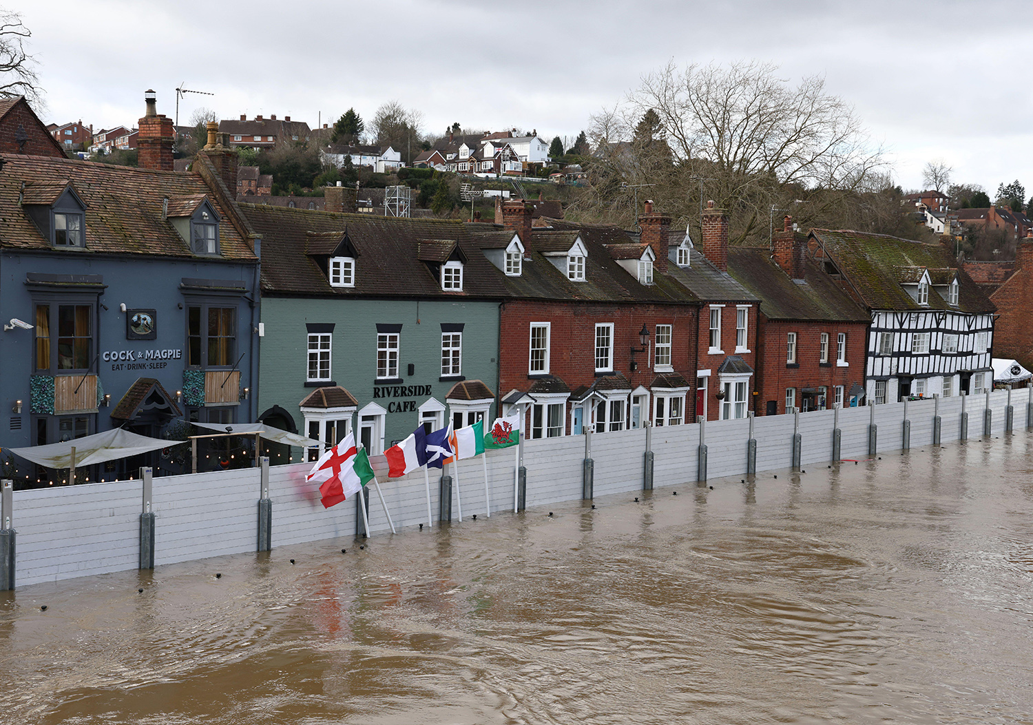 Flood water in front of a metal barrier with restaurants and houses behind.