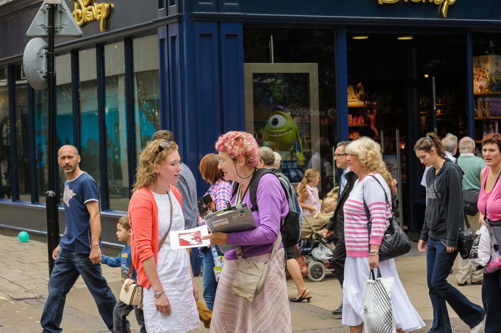 A woman with a clipboard questions a young woman whilst doing a survey in a UK city centre.