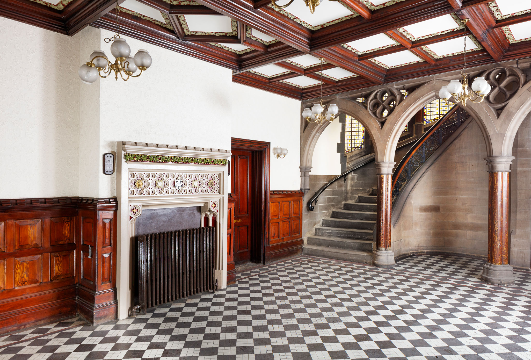 Interior view, showing part of a Victorian gothic style hall and stair; in the hall there is wooden panelling to the lower part of the wall and a decorated fireplace.
