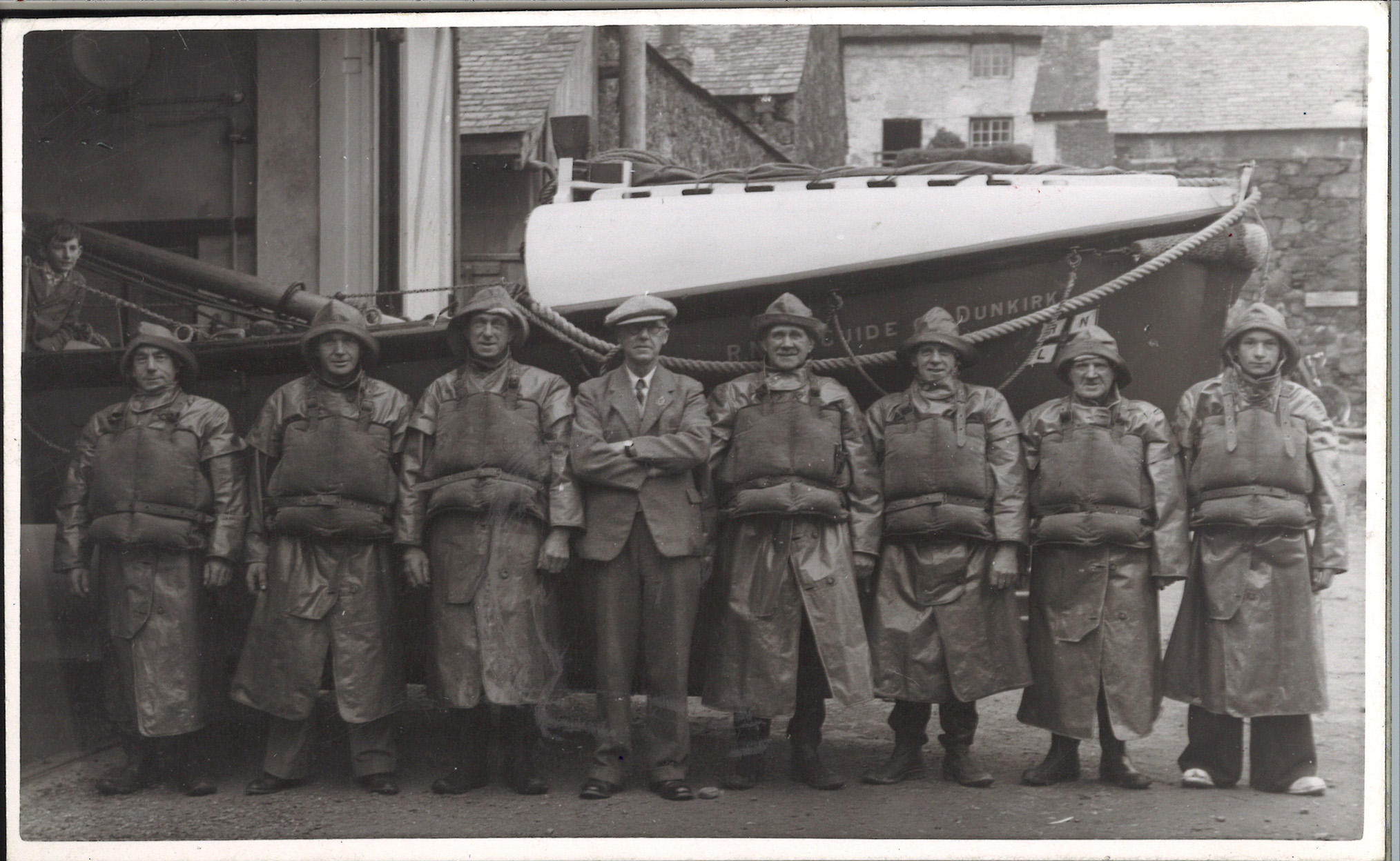 A black and white photograph of a lifeboat crew stood posing in a line in front of a lifeboat