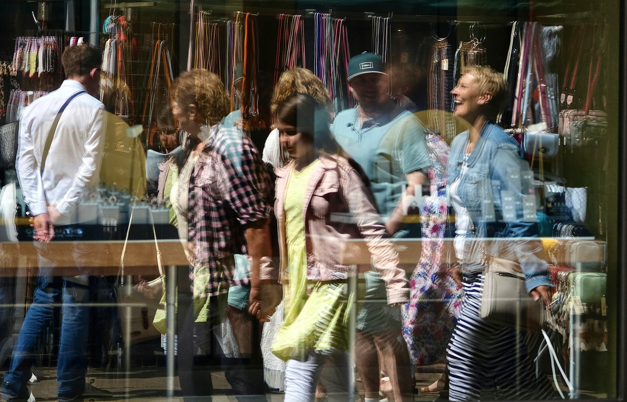 A shop window reflection of people browsing market stalls