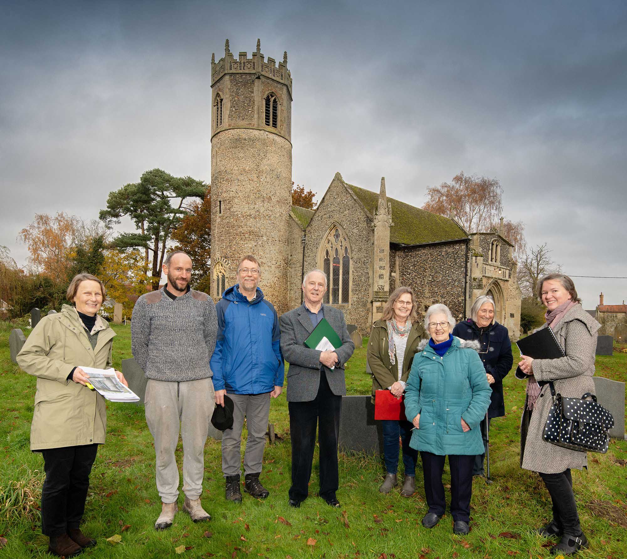 A group of men and women standing in front of a church with a bell tower