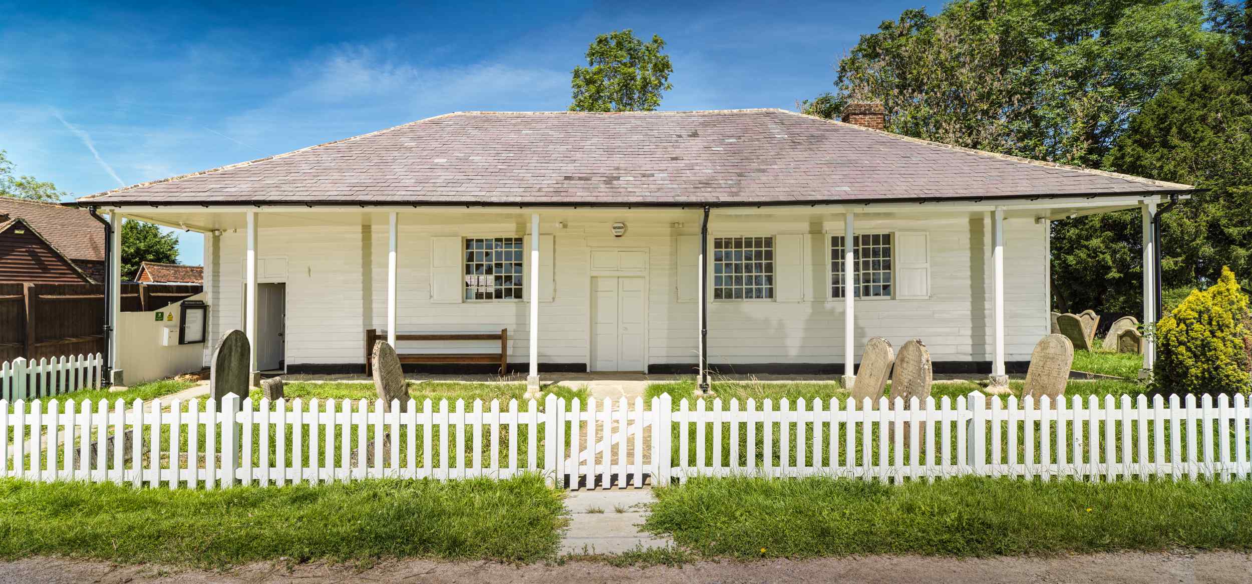 Simple white single-story, wooden-clad building with grey tiled roof and white picket fence in front.