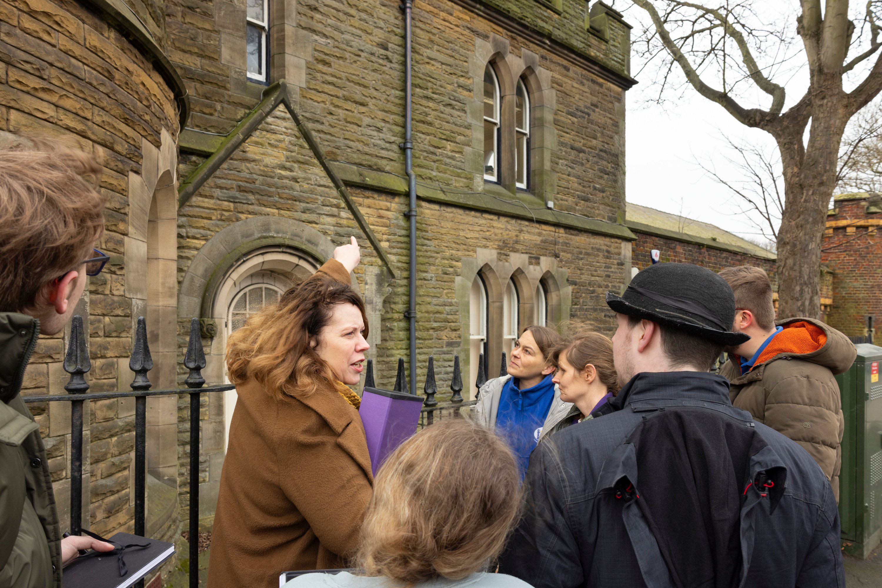 Image shows person pointing to old jail building with other people listening.