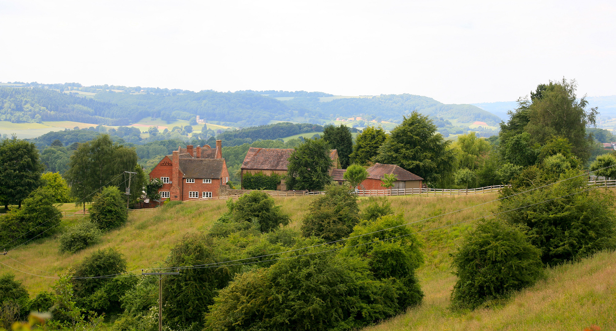 Traditional red brick house and farm buildings set in rolling countryside.