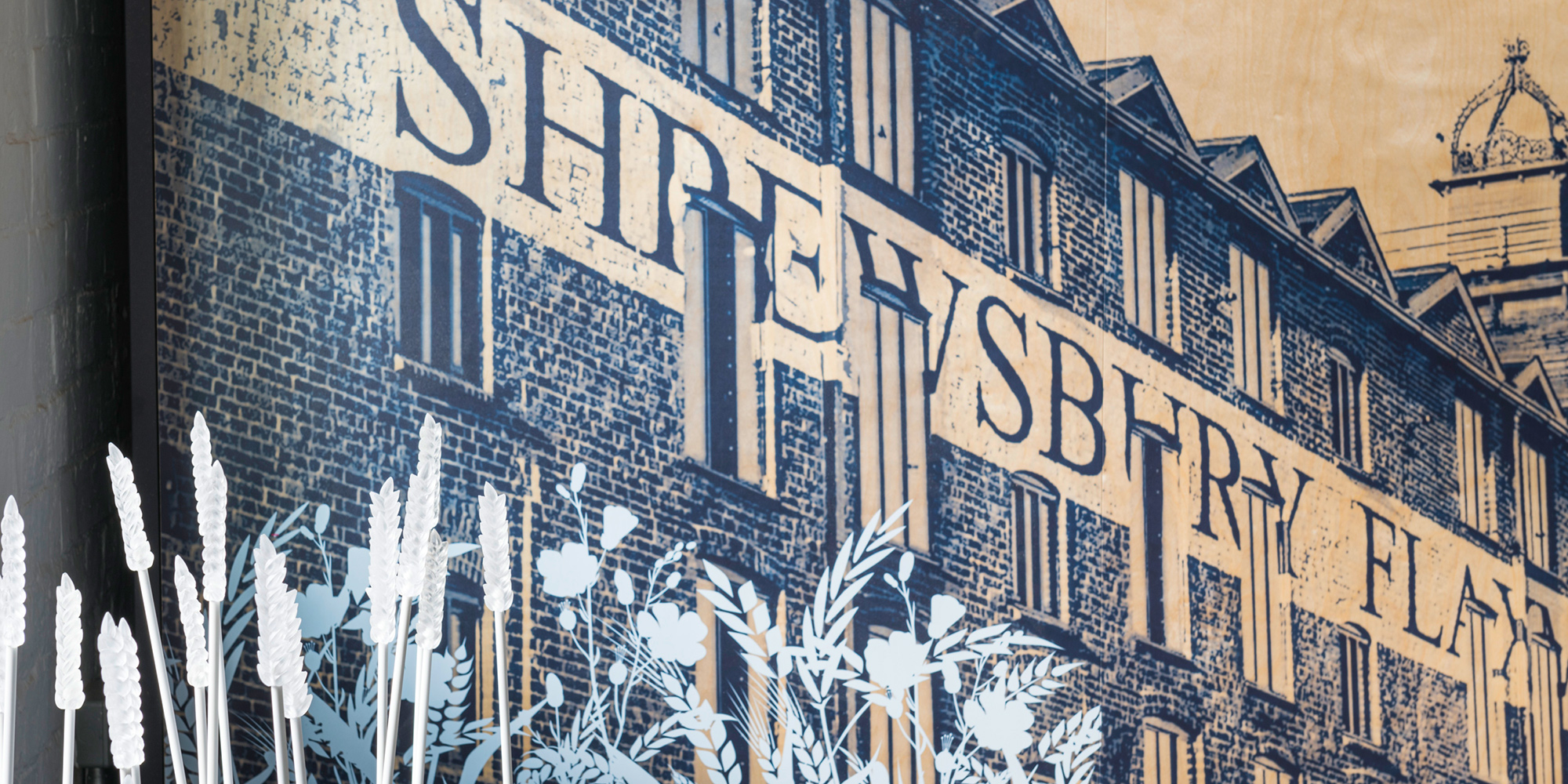 A close-up photo of an exhibition piece with Shrewsbury Flaxmill Maltings rendered in blue and wildflowers in the foreground.