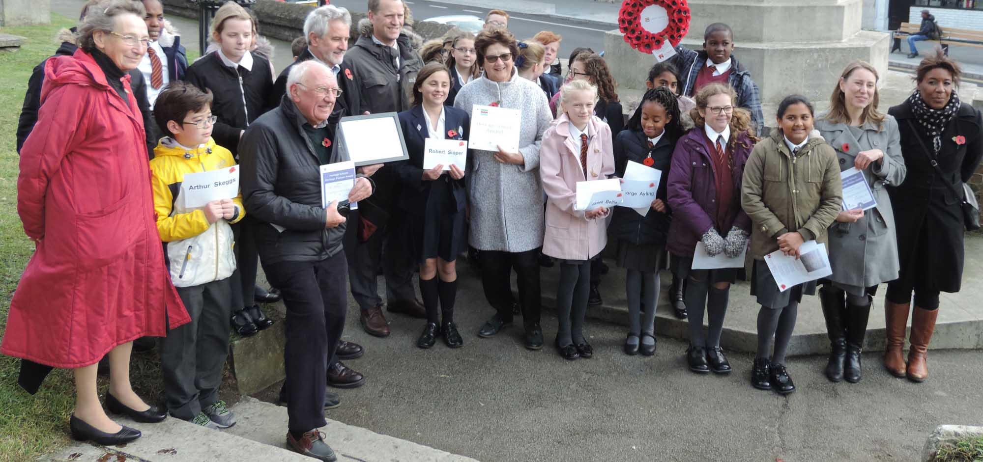Group of children and teachers standing for a group photo in front of a war memorial.