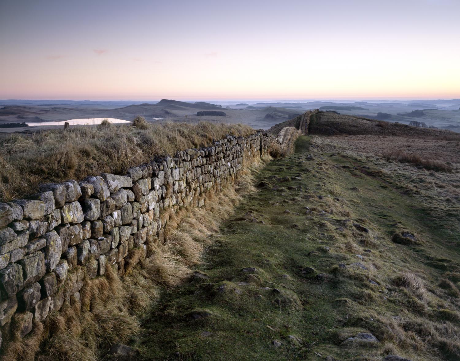 An old stone wall with a grass path alongside leading from the left into the middle distance.