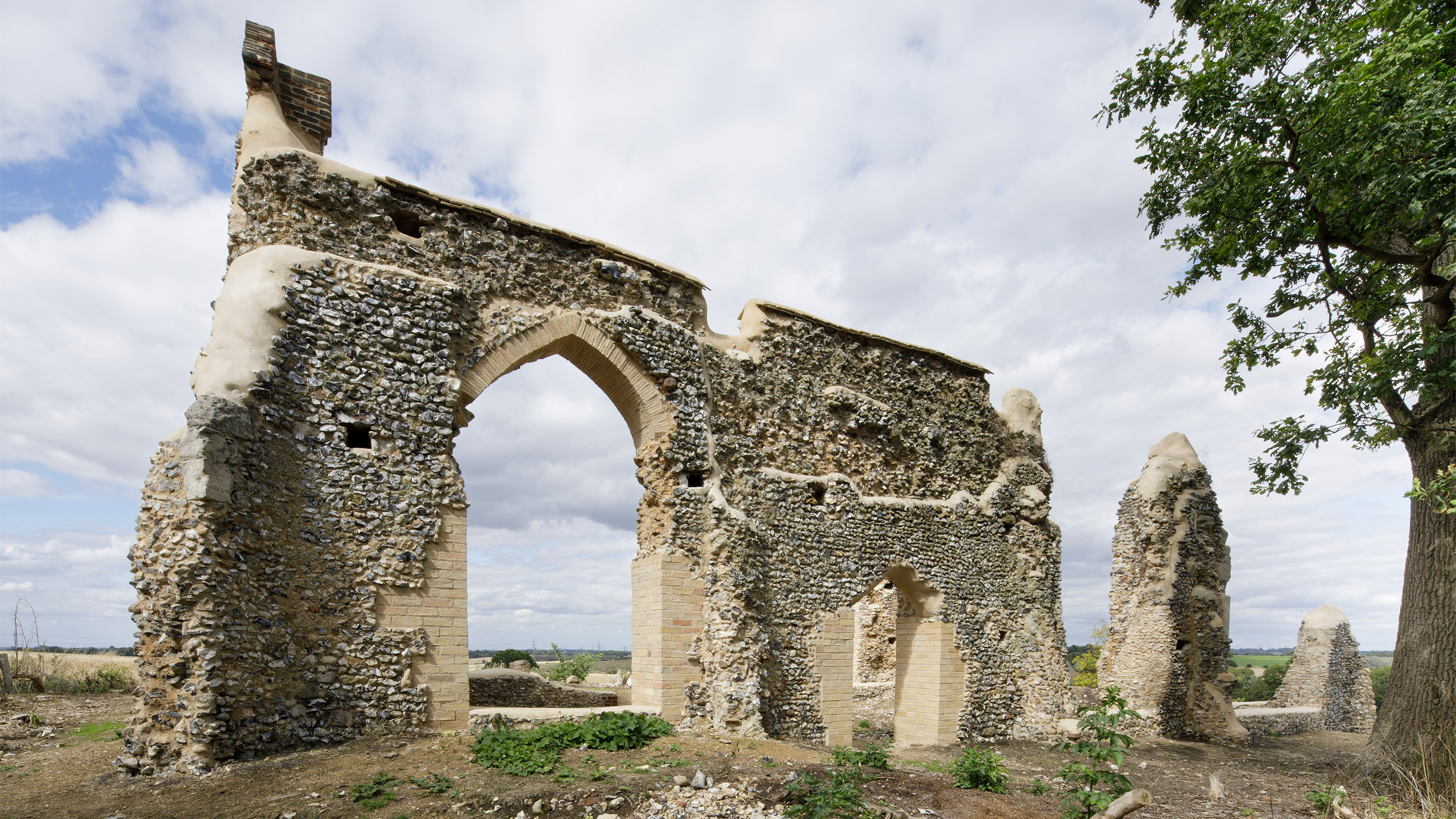 The ruined wall of the chapel shows an arched doorway and a flint-covered wall.