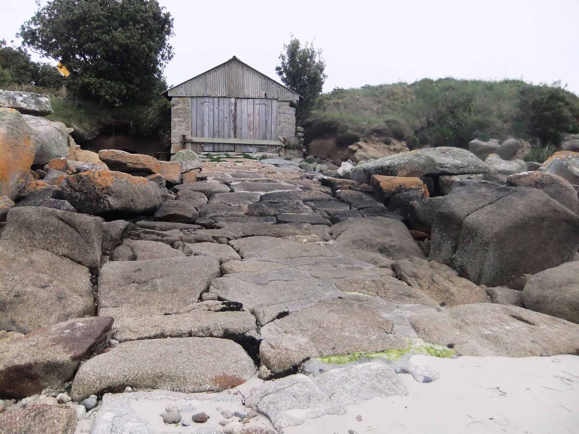 Traditional wooden gig shed at the top of a paved slipway.