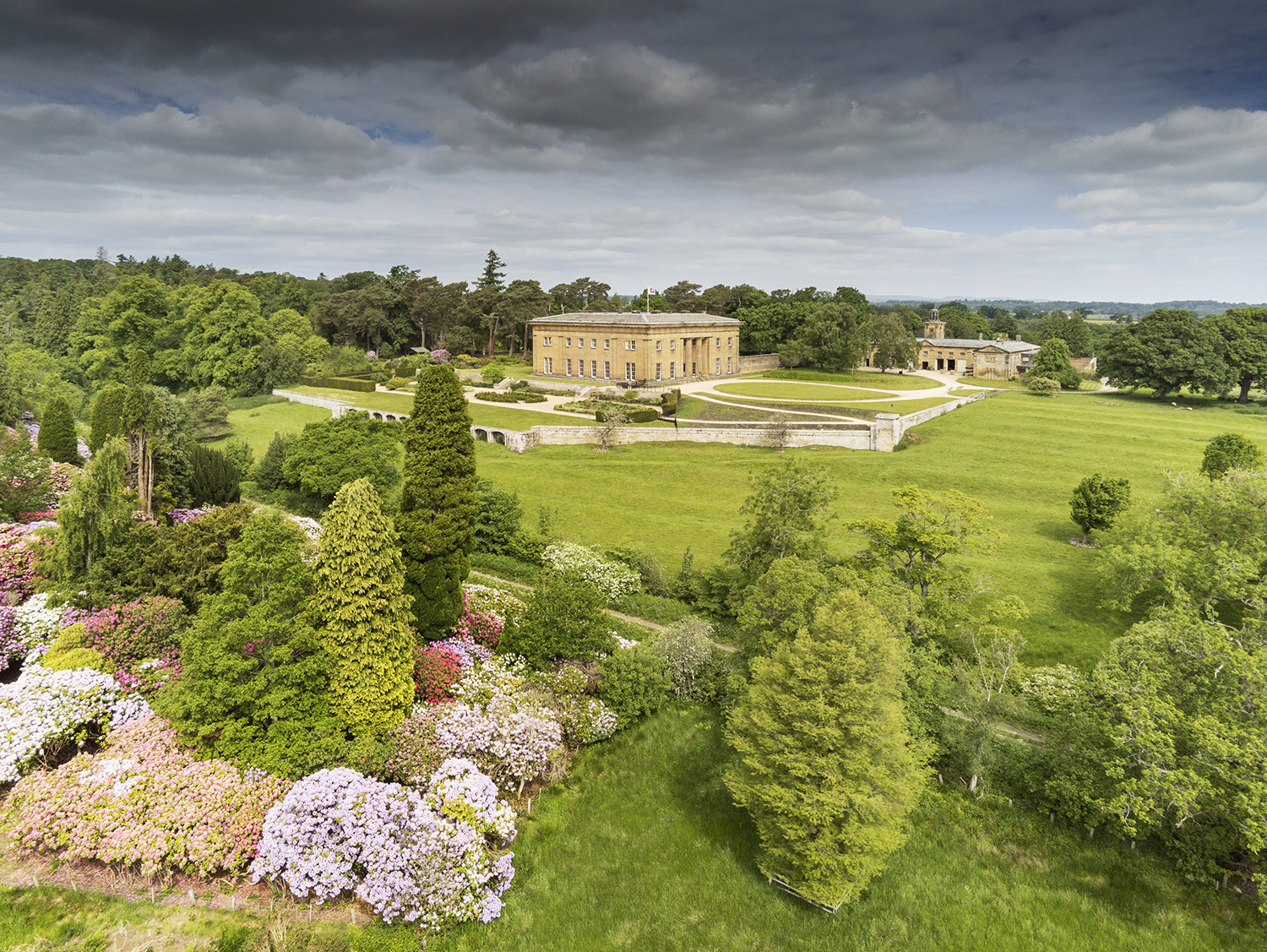 Oblique aerial view of Belsay Hall and its gardens from the south-east, with rhododendron bushes in the foreground