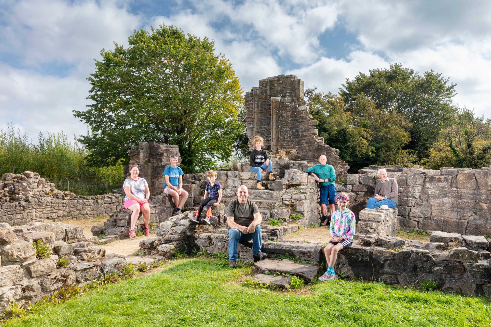 Image of ruins with grass in the foreground and volunteers sitting on the walls.