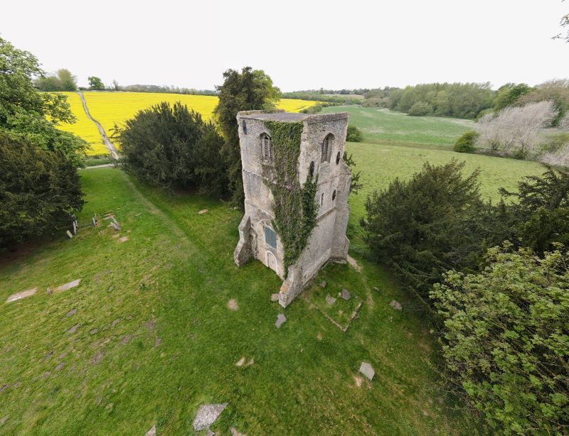 Aerial view of a 3-storey stone church tower among trees and fields