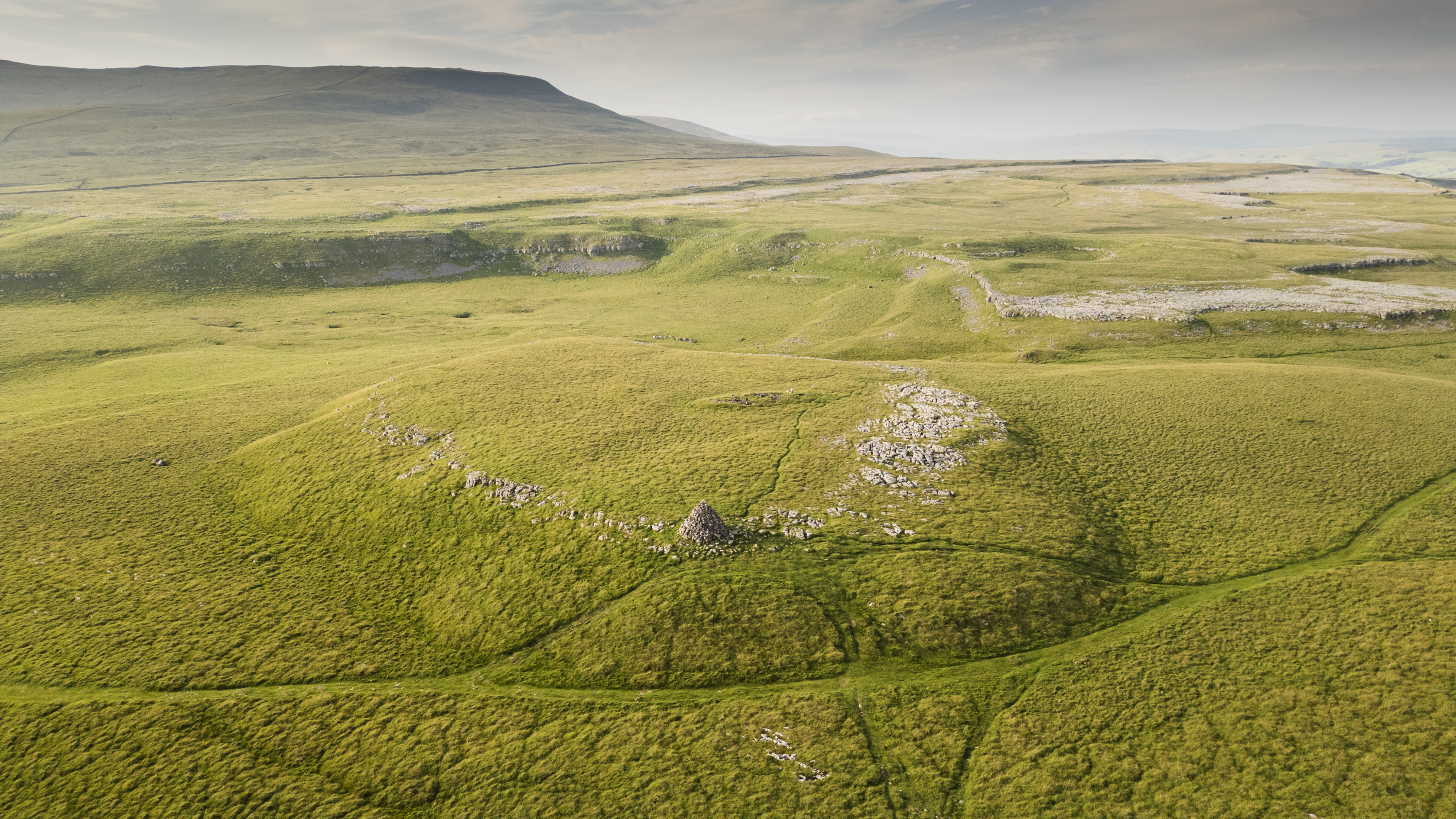 A rocky, grassy large mound with hills in the background.