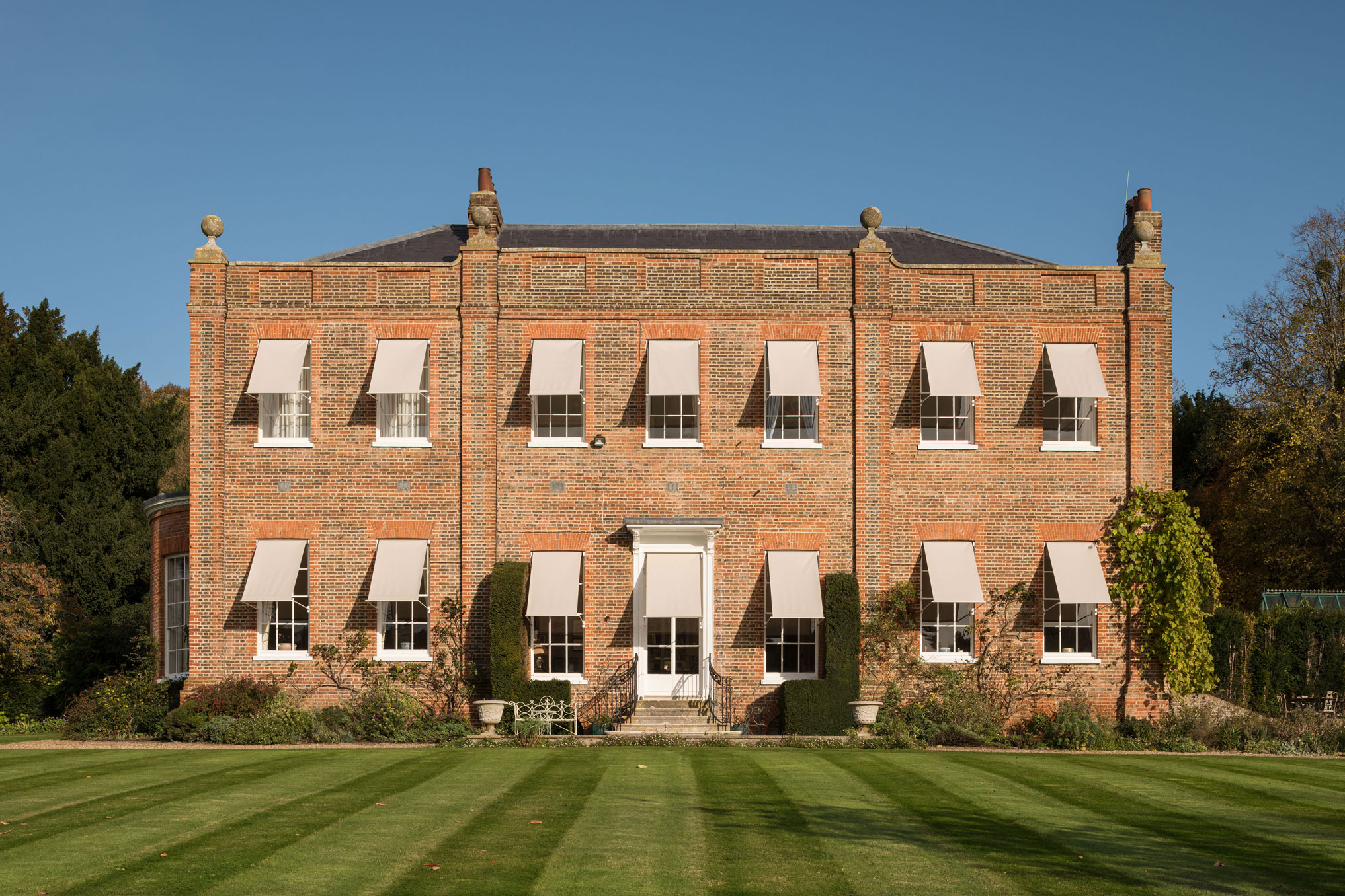 The elevation of a 2-storey country house built of red brick, showing awnings to each of the windows and to the garden entrance door.