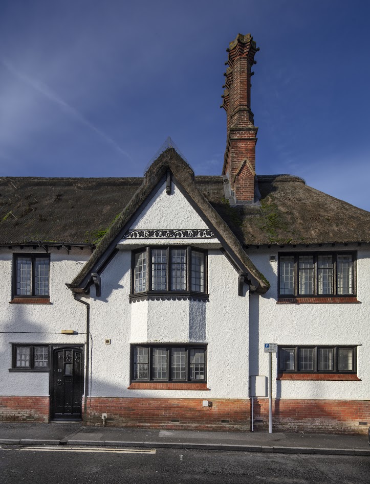 The top part of the former Lloyds bank building shows a whitewashed front, leaded windows, grapevine decoration and thatched roof.