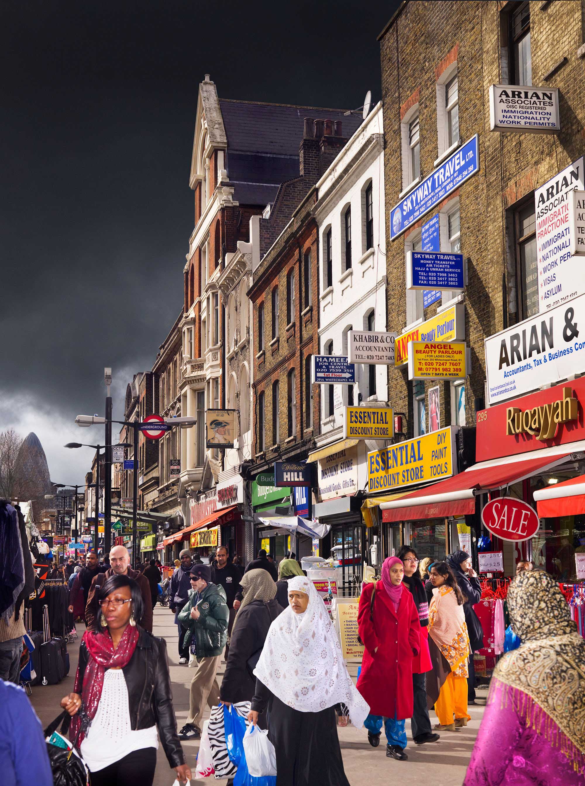 General view looking west along the north side of Whitechapel Road near Brady Street, busy with pedestrians and shoppers, showing signage and shop fronts, and with 'The Gherkin' in the distance
