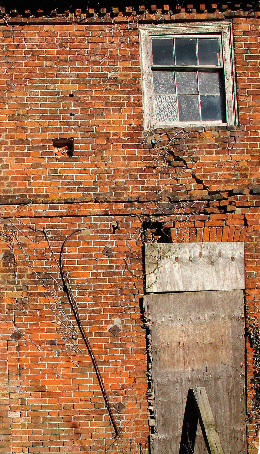 A damaged window in a red brick wall.