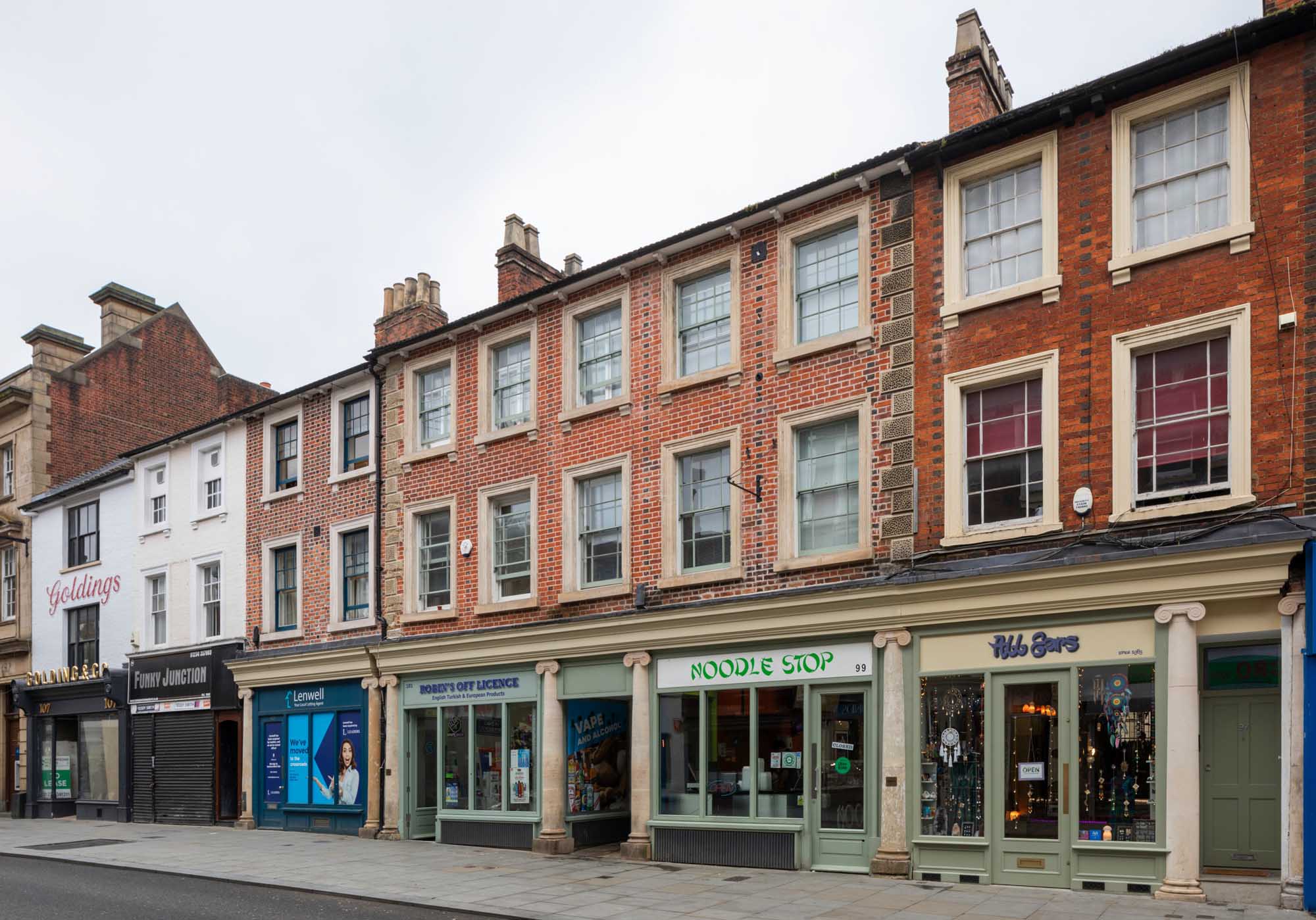 A three-storey terrace of brick buildings with shops on the ground floor.