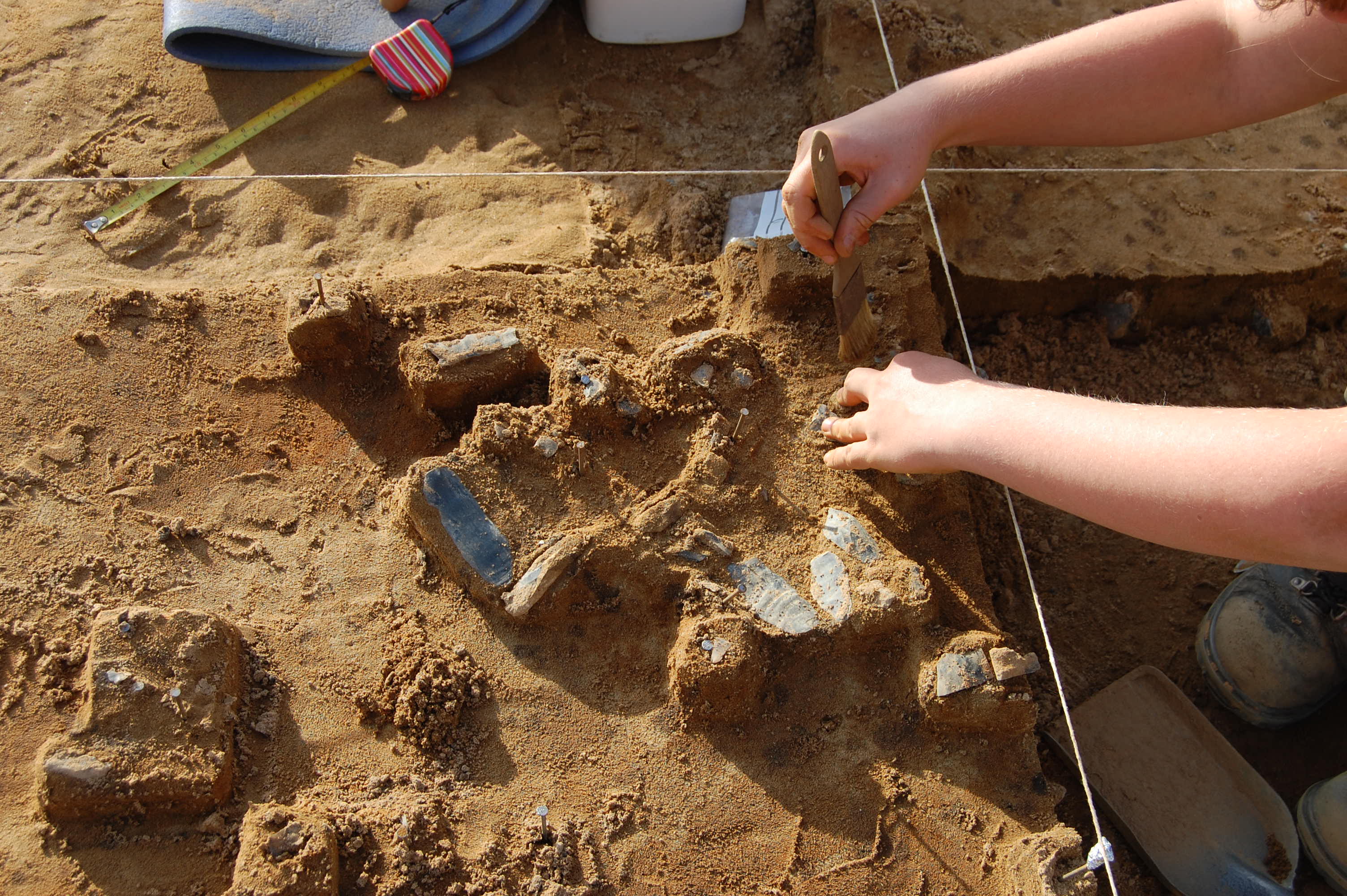 Close-up photo showing hand-excavation of lithic artefacts in a sandy matrix